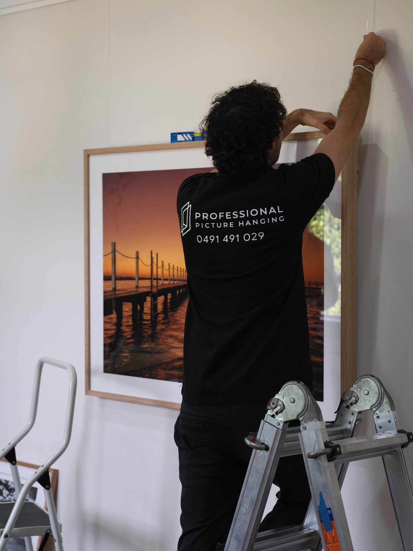 Professional Picture Hanging installer levelling a framed artwork on a rail system